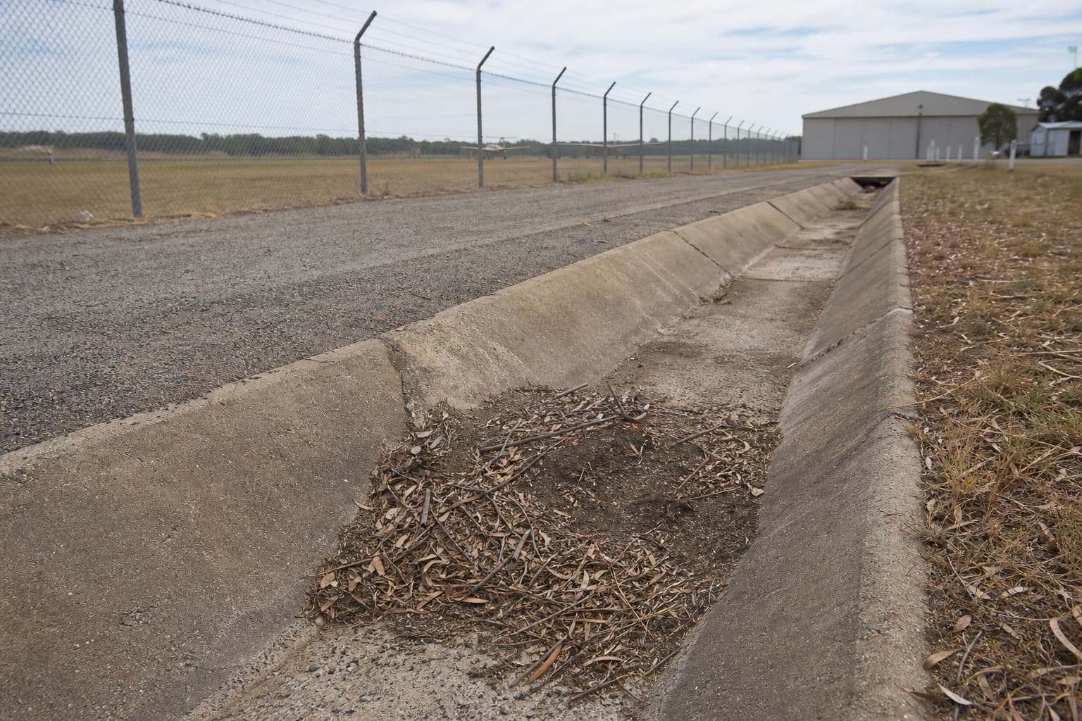 Long open concrete drainage channel beside an airport service area.